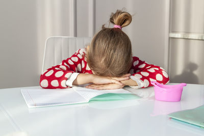 Rear view of girl sitting on table at home