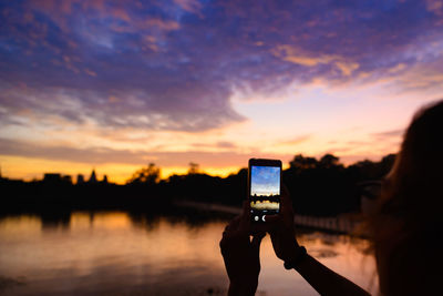 Man photographing through smart phone against sunset sky