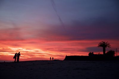 Silhouette of people on beach against cloudy sky