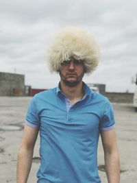 Portrait of man wearing wig while standing against sky