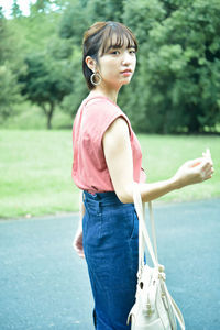 Side view of young woman standing against trees