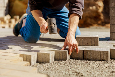 Young man laying gray concrete paving slabs in house courtyard on gravel foundation base. 