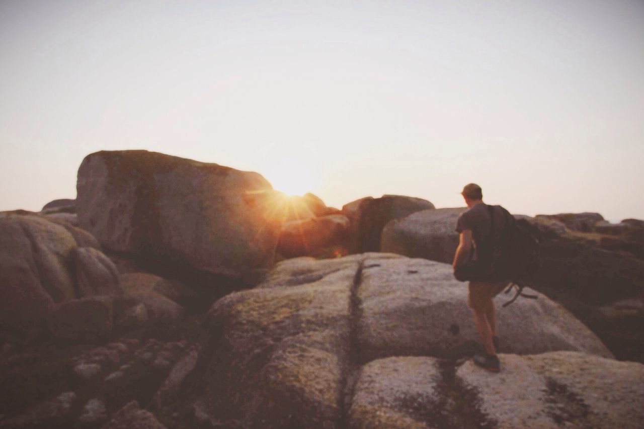 clear sky, copy space, rock - object, men, lifestyles, full length, leisure activity, sunset, tranquility, sun, rock formation, tranquil scene, nature, landscape, standing, scenics, sunlight, beauty in nature