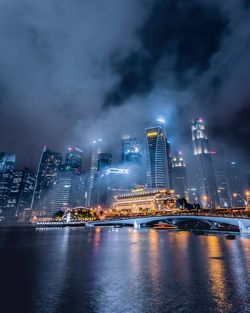 Illuminated buildings by river against sky at night