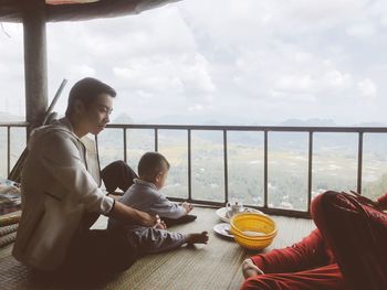 Men sitting by window against sky