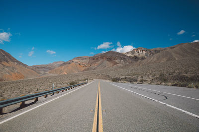Empty road amidst mountains against blue sky