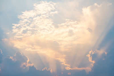 Low angle view of sunlight streaming through clouds