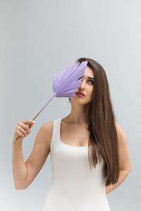 Attractive brunette woman hides face behind purple exotic plant leaf in studio