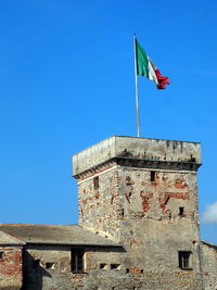 Low angle view of flag on building against clear blue sky