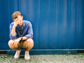 Depressed man crouching against blue wall