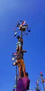 Low angle view of people against clear blue sky