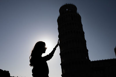 Optical illusion of silhouette woman holding leaning tower of pisa against clear sky