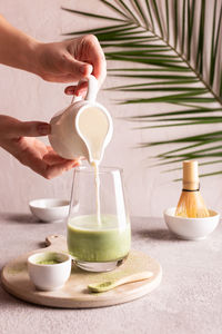 Woman pouring milk into a glass with green tea matcha