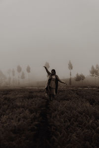 Rear view of woman standing on field against sky