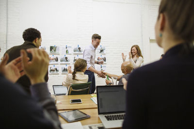 Business people applauding for businessman giving handshake to male colleague in board room