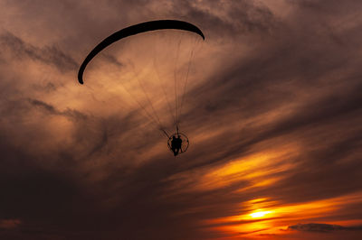 Low angle view of person paragliding against sky during sunset