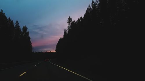 Road amidst silhouette trees against sky at sunset