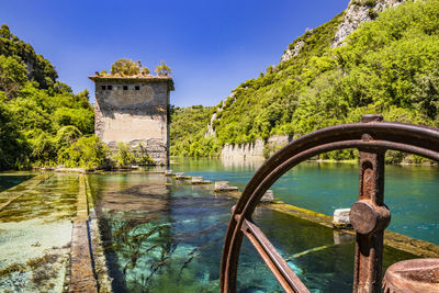 Built structure by river against clear blue sky