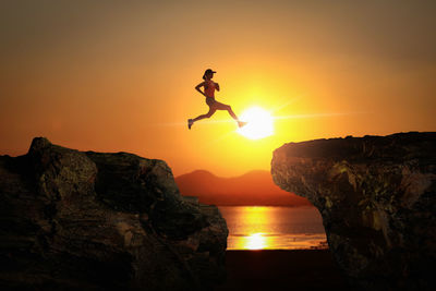 Low angle view of man jumping on rock at sunset