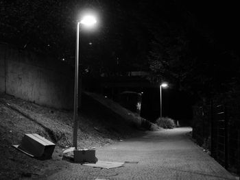 Illuminated street light by road against sky at night