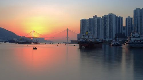 Bay by buildings in city against sky during sunset