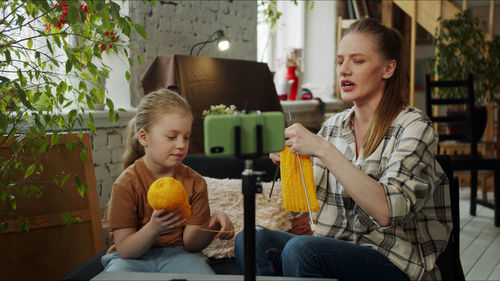 Mother and daughter crocheting while learning from mobile phone at home