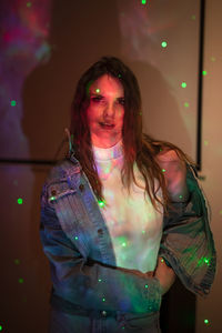 Portrait of smiling young woman standing against illuminated wall