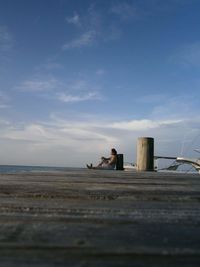 Man sitting on beach by sea against sky