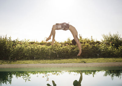 Man somersaulting into swimming pool against clear sky