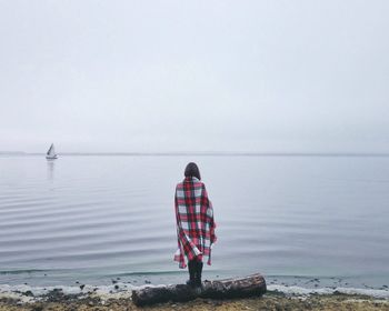 Rear view of woman standing at sea shore during foggy weather
