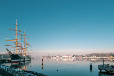 Sailboats moored at harbor against clear sky