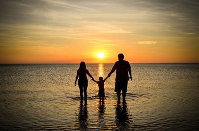 Silhouette family standing at beach against sky during sunset