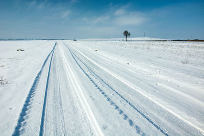 Road covered with snow, wheel tracks, horizon and blue sky