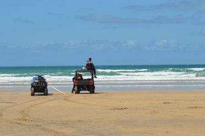 People riding motorcycle on beach against sky