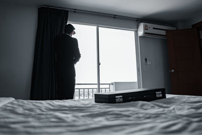 Rear view of man standing on bed at home