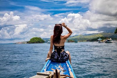 Rear view of woman sitting in boat on sea against sky
