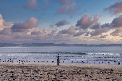 Woman standing with arms raised surrounded by seagulls on sand at beach