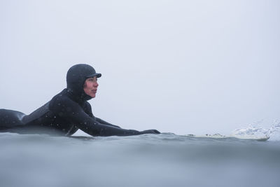 Young man in sea against clear sky during winter