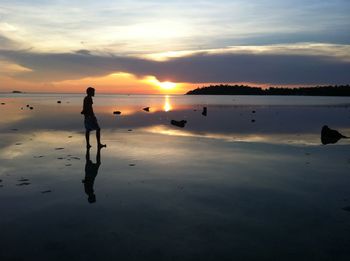 Silhouette man standing on beach against sky during sunset