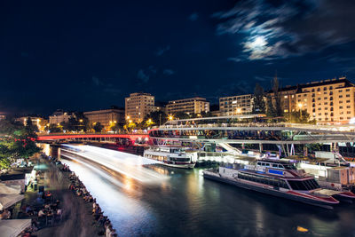 Light trails on street by illuminated buildings in city at night