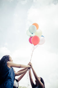 Low angle view of woman holding balloons against sky