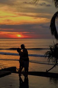 Side view of couple standing at beach during sunset