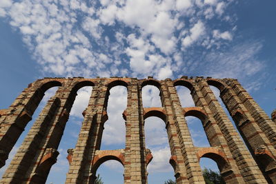 Low angle view of old ruin, roman aqueduct against blue sky with white clouds.