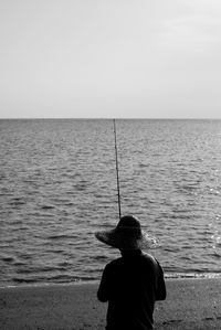Rear view of man fishing in sea against clear sky