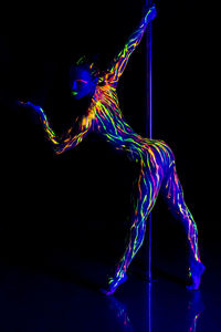 Full length of woman wearing neon clothing doing pole dance against black background