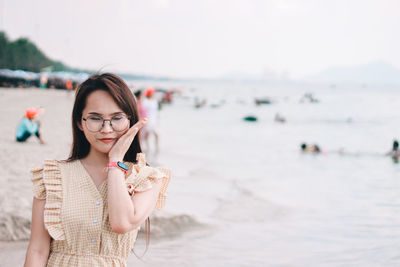 Beautiful woman wearing sunglasses gesturing while standing at beach