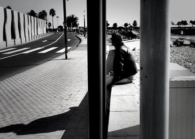 Man sitting on retaining wall by street against clear sky