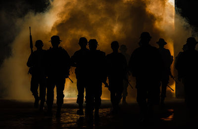 Silhouette army soldiers with guns walking by towards smoke 