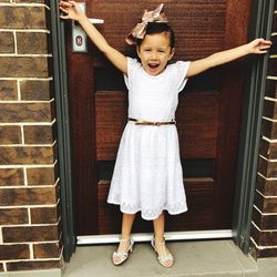 Full length portrait of cute girl standing against brick wall