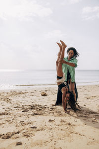 Mother supporting daughter while doing handstand on sand at beach